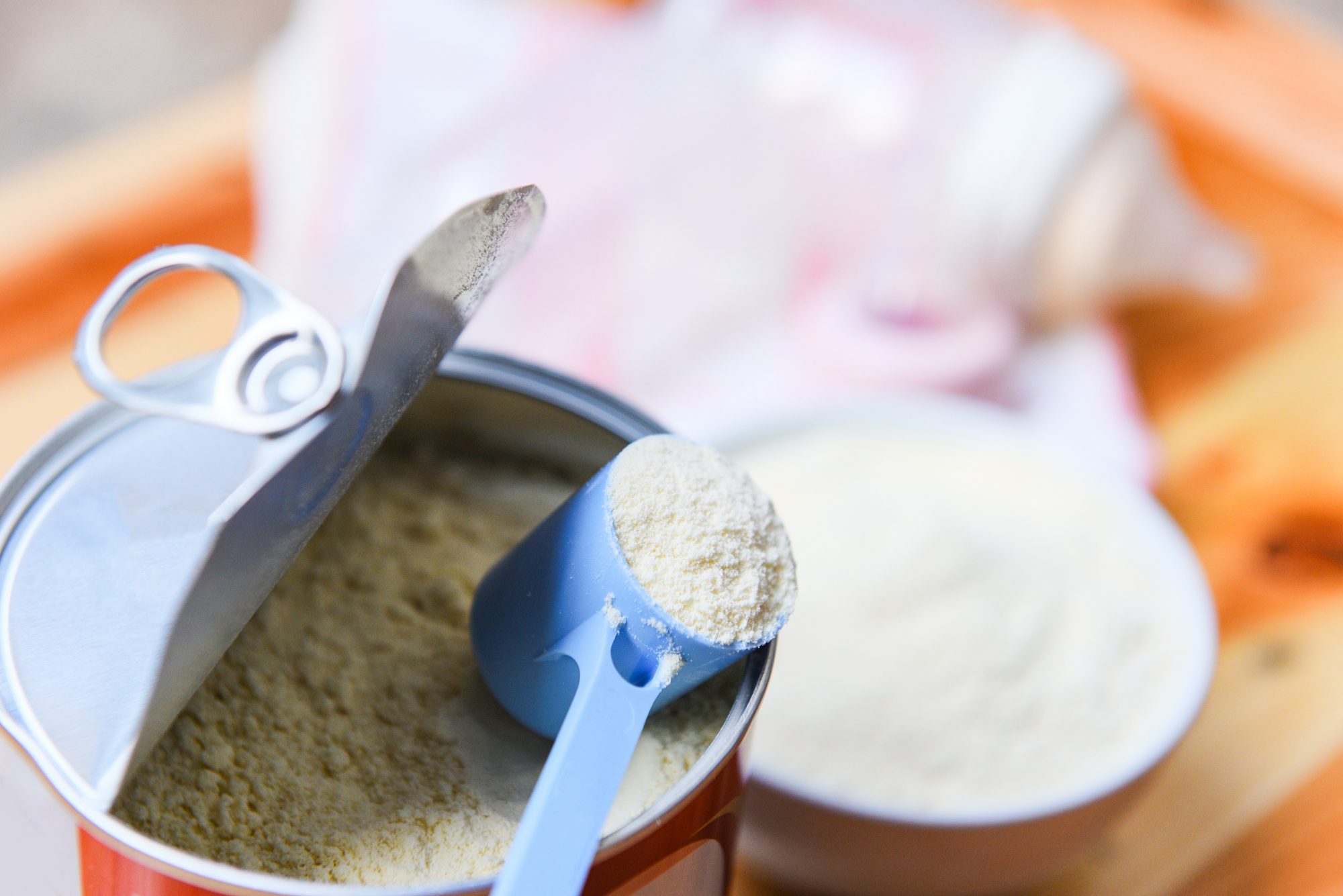 An image of baby formula in a spoon on top of a can with a milk bottle.