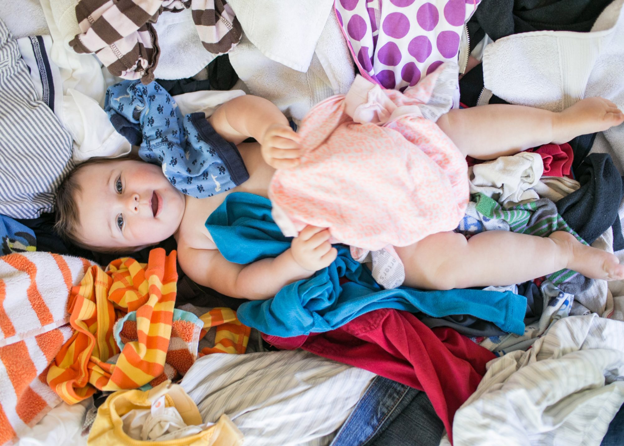 An image of a baby surrounded by baby clothes.