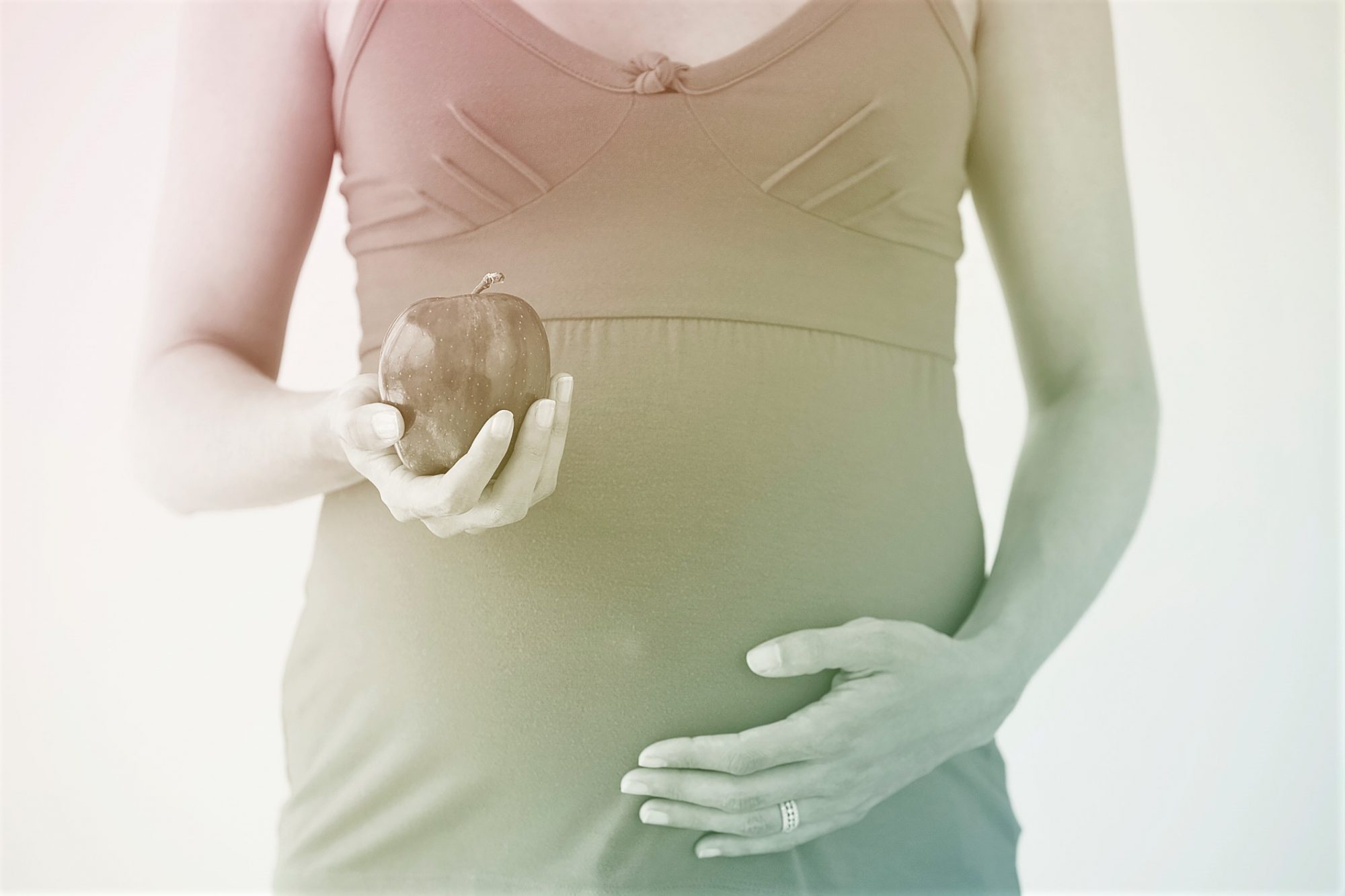 Pregnant woman holding apple in one hand and touching belly with other hand