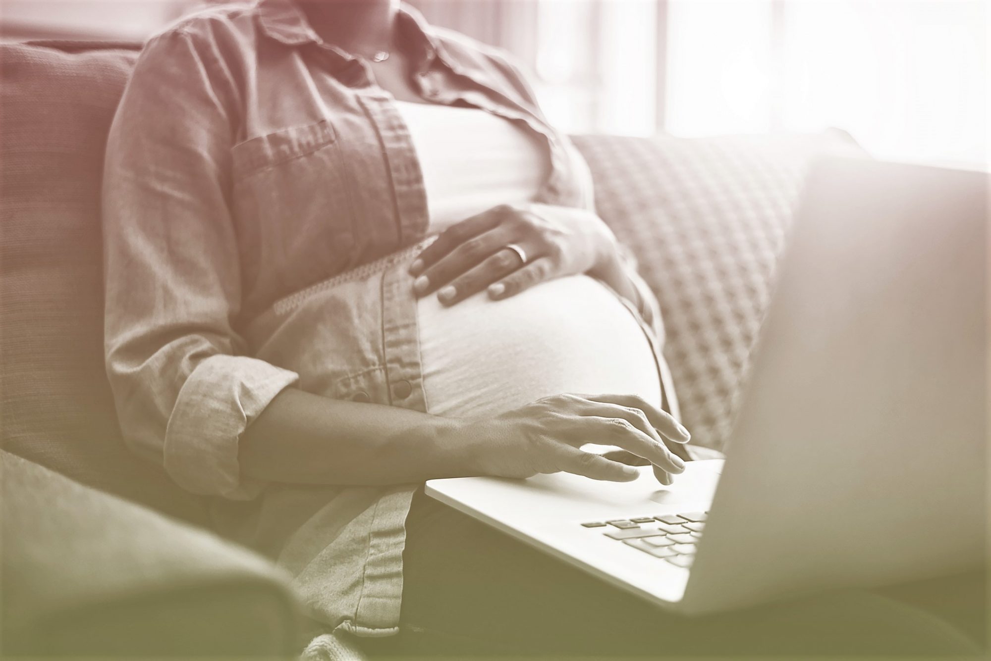 Pregnant woman with hand on belly using laptop