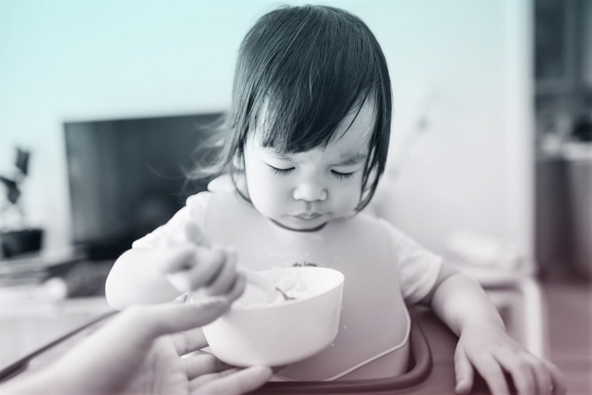 Asian toddler girl sitting on high chair feeding herself at home