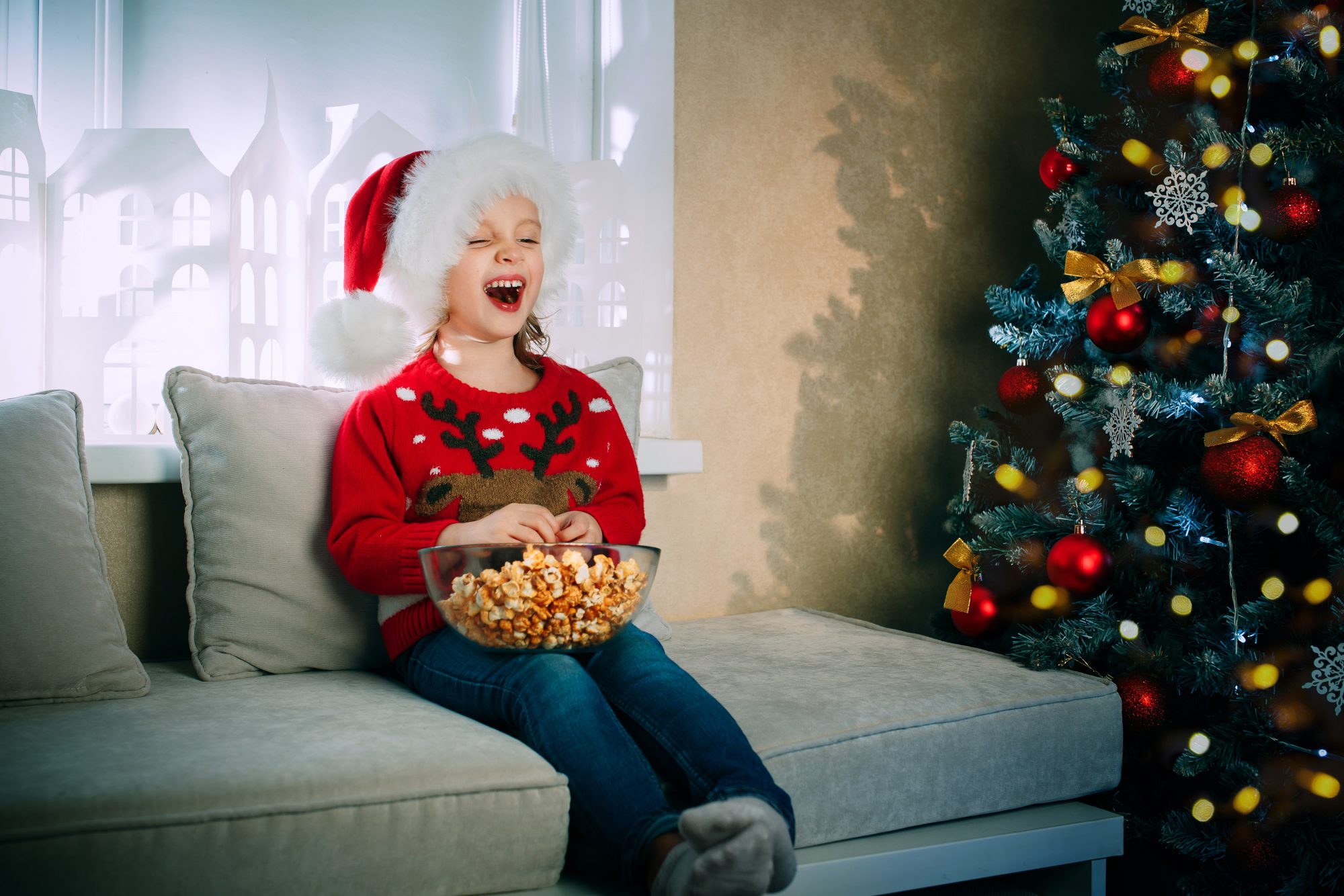 An image of a girl in a Santa Claus hat while watching TV.