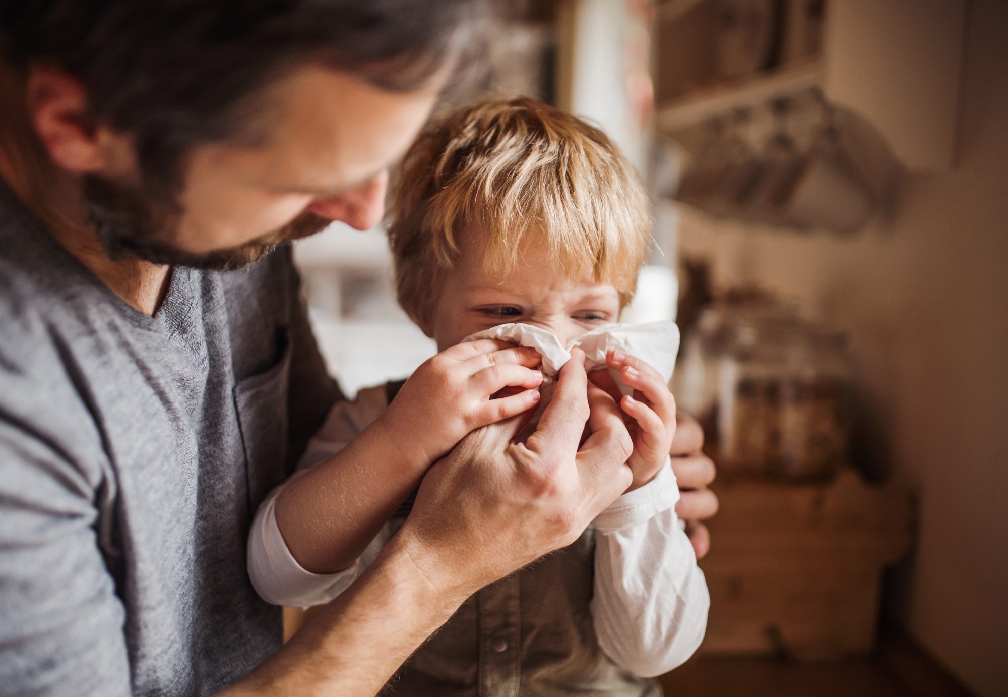 An image of a dad helping his son blow his nose.