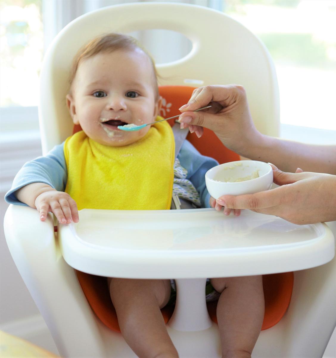 Baby Eating Infant Cereal In High Chair