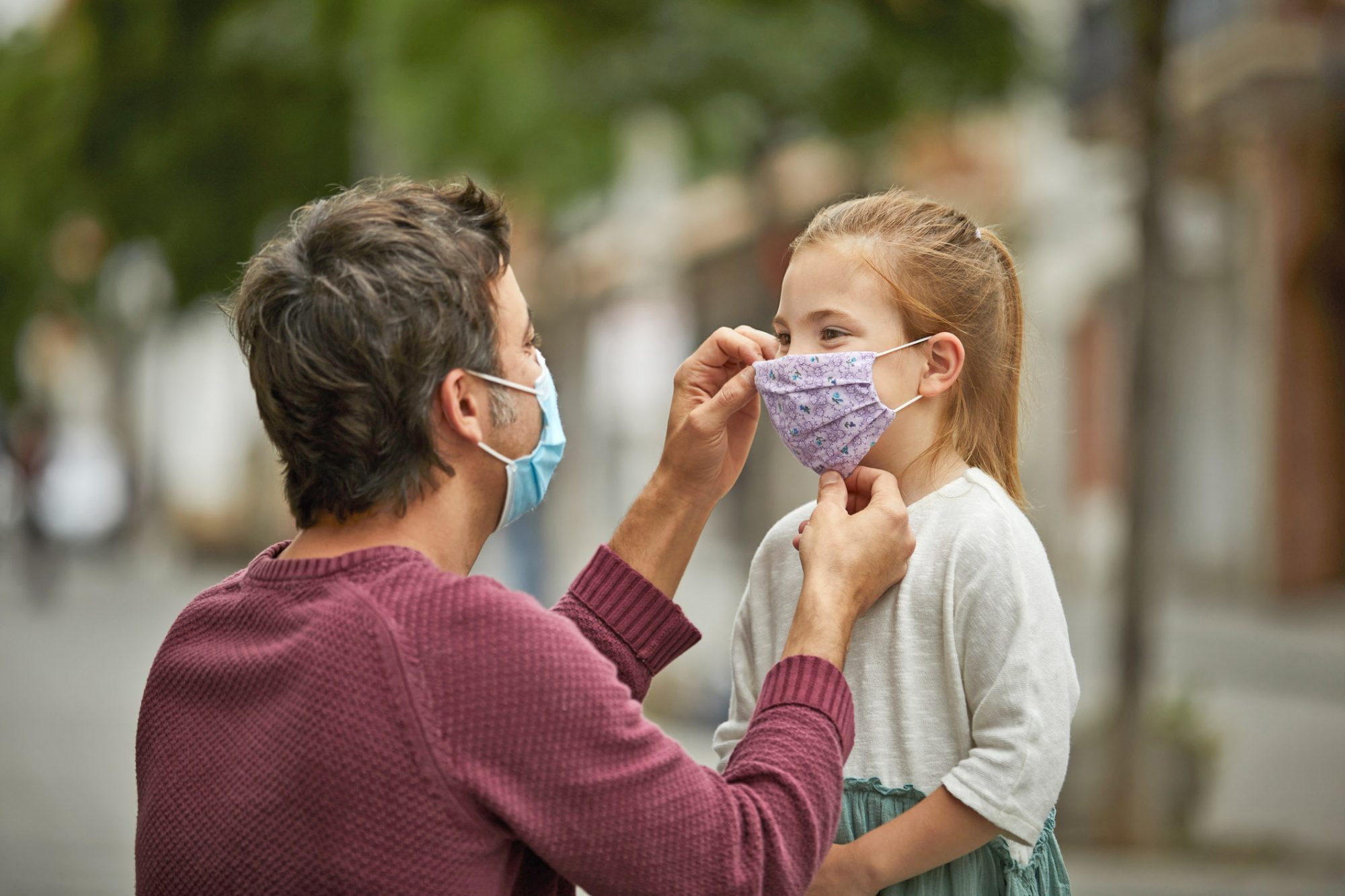 An image of a father putting a mask on his daughter.