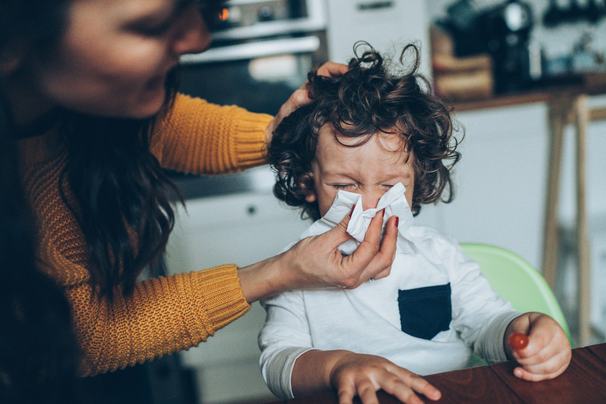 An image of a mom helping a child blow their nose.