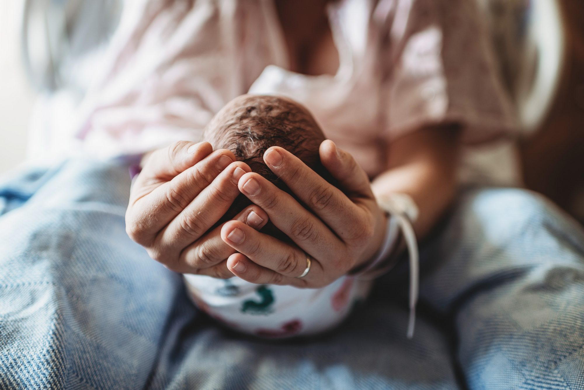 An image of a mother's hands holding her newborn baby's head.