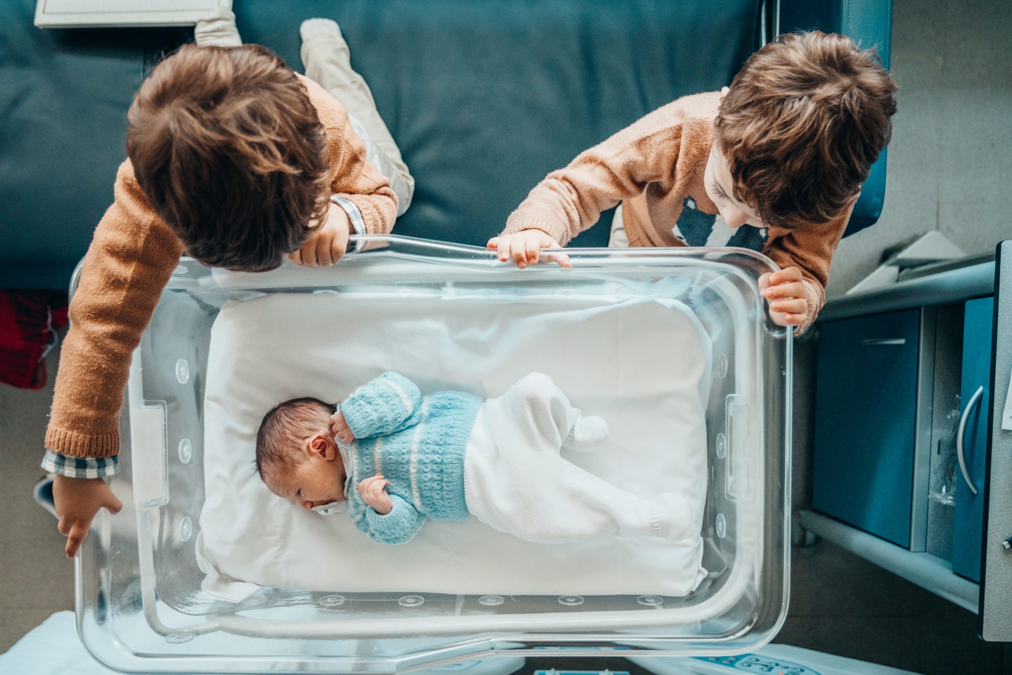 An image of two brothers looking at a new baby.