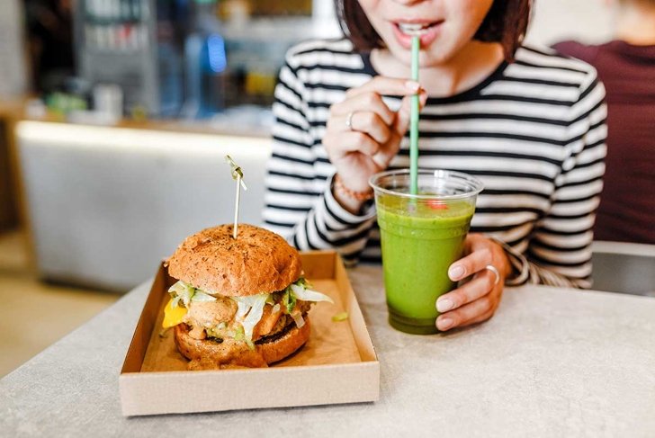 A young woman drinks green smoothies and eats a burger in a vegan fast food restaurant