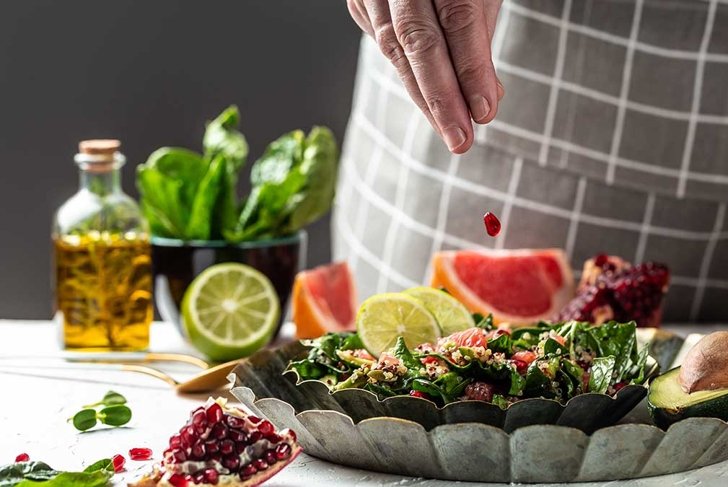 Freezer food prepare in process vegan winter salad by chef hand in home kitchen with quinoa, spinach, avocado, grapefruit, pomegranate, nuts and microgreens.